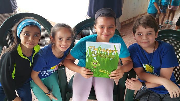 Four children sitting together, one of them holding up a copy of The Hungry Snake.