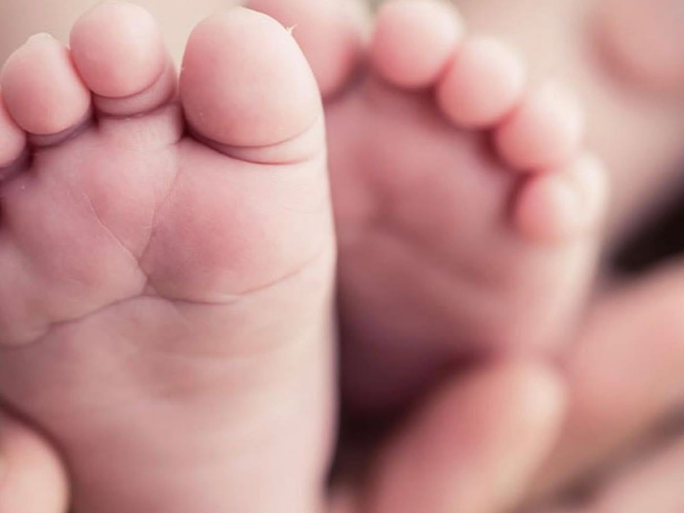 The bare feet of a newborn baby, held in an adult's hands.